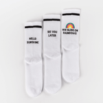 Socken-Bundle mit drei Designs: HELLO SUNSHINE, SKI YOU LATER und WE SLIDE ON RAINBOWS mit Regenbogenmotiv, flach nebeneinander liegend.