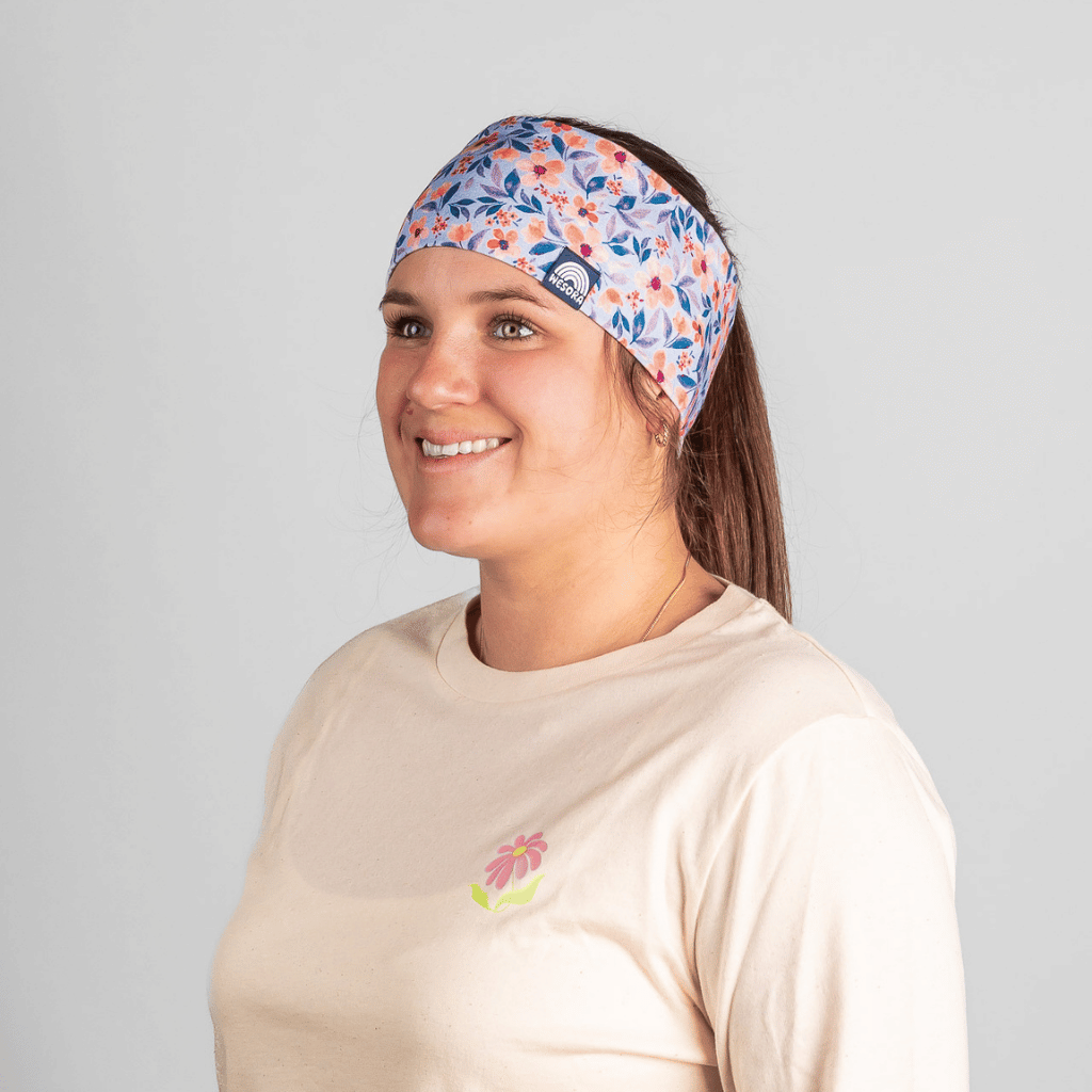 Stirnband - Wildflower mit floralem Muster, getragen von junger Frau, die lächelnd zur Seite schaut, vor neutralem Hintergrund.
